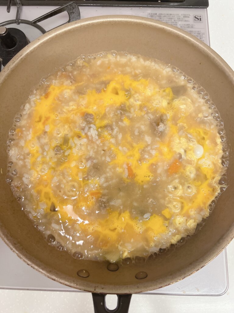 豚汁雑炊に卵を入れて仕上げている様子